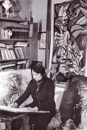 Die „malbesessene" Jeanne Mammen in ihrem Atelier, um 1945, hinter ihr das Gemälde "Der Würgeengel", (um 1939–1942), Foto: Archiv Förderverein der Jeanne-Mammen-Stiftung e.V.